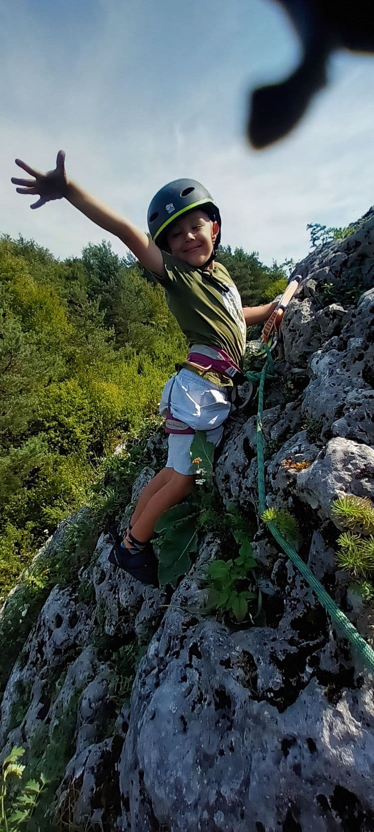 Chłopiec na skale z uniesioną ręką, uśmiechnięty
